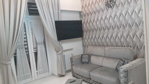 A living room with a sofa, a flat-screen TV, a decorative wall, and a window with curtains. - Central Station House (Naples)