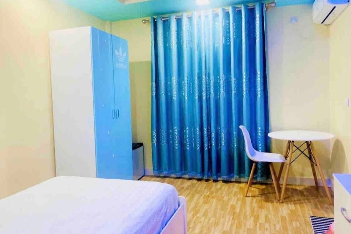 Un dormitorio con cama, una mesita, una silla, un armario y una ventana con cortinas azules.