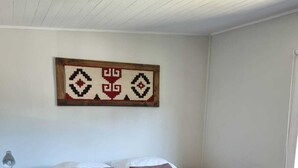 A bedroom with a large bed, a nightstand with a lamp, and a wall-mounted artwork. - Hostal Irma (Pucon)