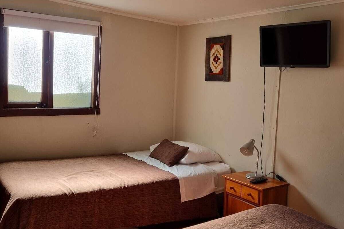 A room with two beds, a TV, a desk with a lamp, and a window with blinds.