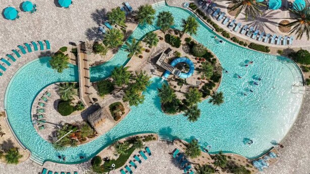 An aerial view of a resort with a winding pool, sun loungers, and palm trees. - ChampionsGate Luxury 8BR Villa, Pool, Theater, Game Room (Four Corners)