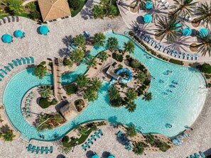 An aerial view of a resort with a winding pool, sun loungers, and palm trees.