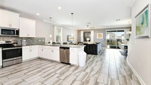 A modern kitchen with white cabinets, stainless steel appliances, and a herringbone-patterned floor. - ChampionsGate Luxury 8BR Villa, Pool, Theater, Game Room (Four Corners)