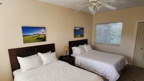 A hotel room with two single beds, a ceiling fan, a window with blinds, and two wall-mounted paintings. - Right Direction Rentals Studio Villa 8270 (Port St. Lucie)