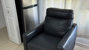 Una habitació amb una cadira de cuir negre, un refrigerador d'acer inoxidable i un rellotge a la paret.
