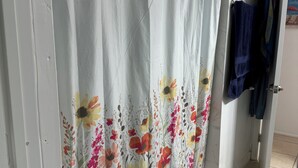 Un bany amb cortina de dutxa amb dibuixos florals, un penjador amb una tovallola blava i una catifes amb disseny al sòl.