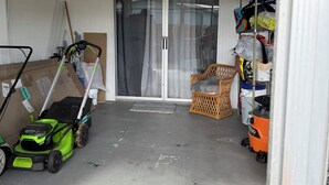 Un garatge amb un mànec de màquina de tall, una cadira de vimetla i una prestatgeria amb diversos objectes.