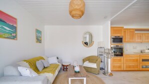 A cozy living room with a sofa, a round table, and a fan. There is a kitchen area with wooden cabinets and appliances. - La Maison Mi Pena - Arcachon basin (Arcachon)