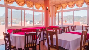 Un restaurant amb taules i cadires rodones, finestres grans amb cortines i vista a les muntanyes.