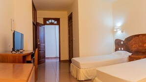 Habitació d'hotel amb dos llits individuals, un escriptori de fusta, televisió i una porta que dóna a una altra habitació.