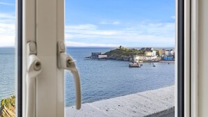 A coastal view through a window with a view of a harbor, buildings, and a lighthouse. - No 10 Croft House (Tenby)