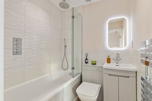 A modern bathroom with a glass-enclosed shower, a white toilet, a sink with a mirror, and a cabinet with toiletries. - 10 Croft House (Tenby)