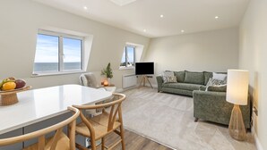 A modern living room with a dining area, a sofa, a TV, and a lamp. - No 10 Croft House (Tenby)