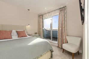 A bedroom with a bed, a chair, a nightstand, and a window with curtains. - 10 Croft House (Tenby)