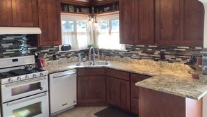 A kitchen with wooden cabinets, a granite countertop, a built-in oven, and a window with curtains. - Spacious 5-bedroom house in beautiful Anaconda with Salt water Hot Tub (Anaconda)