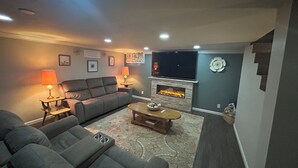 A living room with a fireplace, a sofa, a coffee table, and a TV mounted on the wall. - Spacious 5-bedroom house in beautiful Anaconda with Salt water Hot Tub (Anaconda)