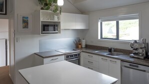 Una cocina moderna con armarios blancos, microondas, estufa y lavavajillas. Hay una ventana que proporciona luz natural y una planta en la encimera.