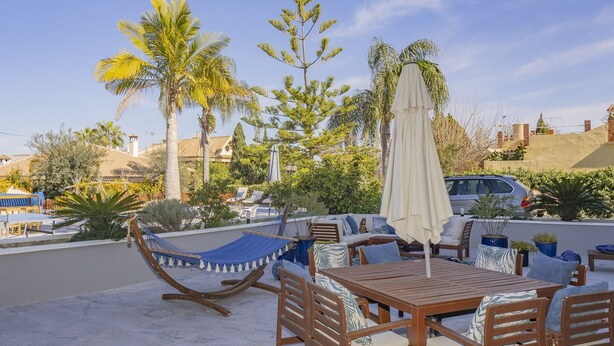 A patio with wooden furniture, a hammock, and a car parked nearby.