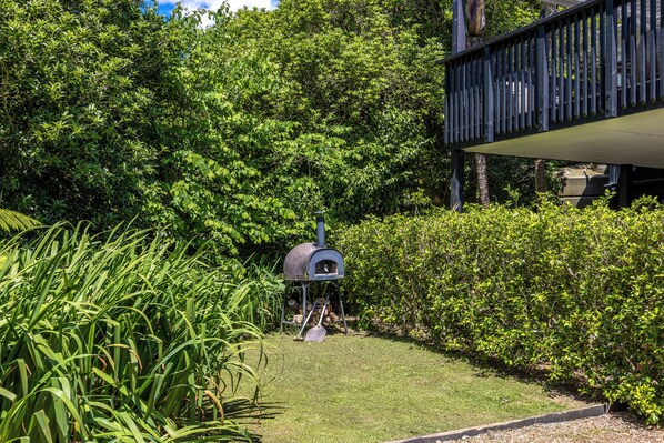 Un jardin agrémenté d’un barbecue, entouré d’une végétation luxuriante et doté d’une terrasse en bois.