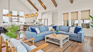 A spacious living room with a large sectional sofa, wooden coffee table, and a dining area with chairs and a kitchen in the background. - Dune Alright 206 PLA (Port Aransas)