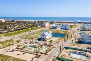 Vista aérea de una zona residencial costera con casas, una piscina y una playa al fondo.