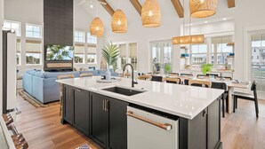 A modern kitchen with a central island, black cabinetry, and a large window overlooking a cityscape. - Dune Alright 206 PLA (Port Aransas)