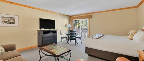 A hotel room with a bed, a desk with a chair, a television, and a sofa.
