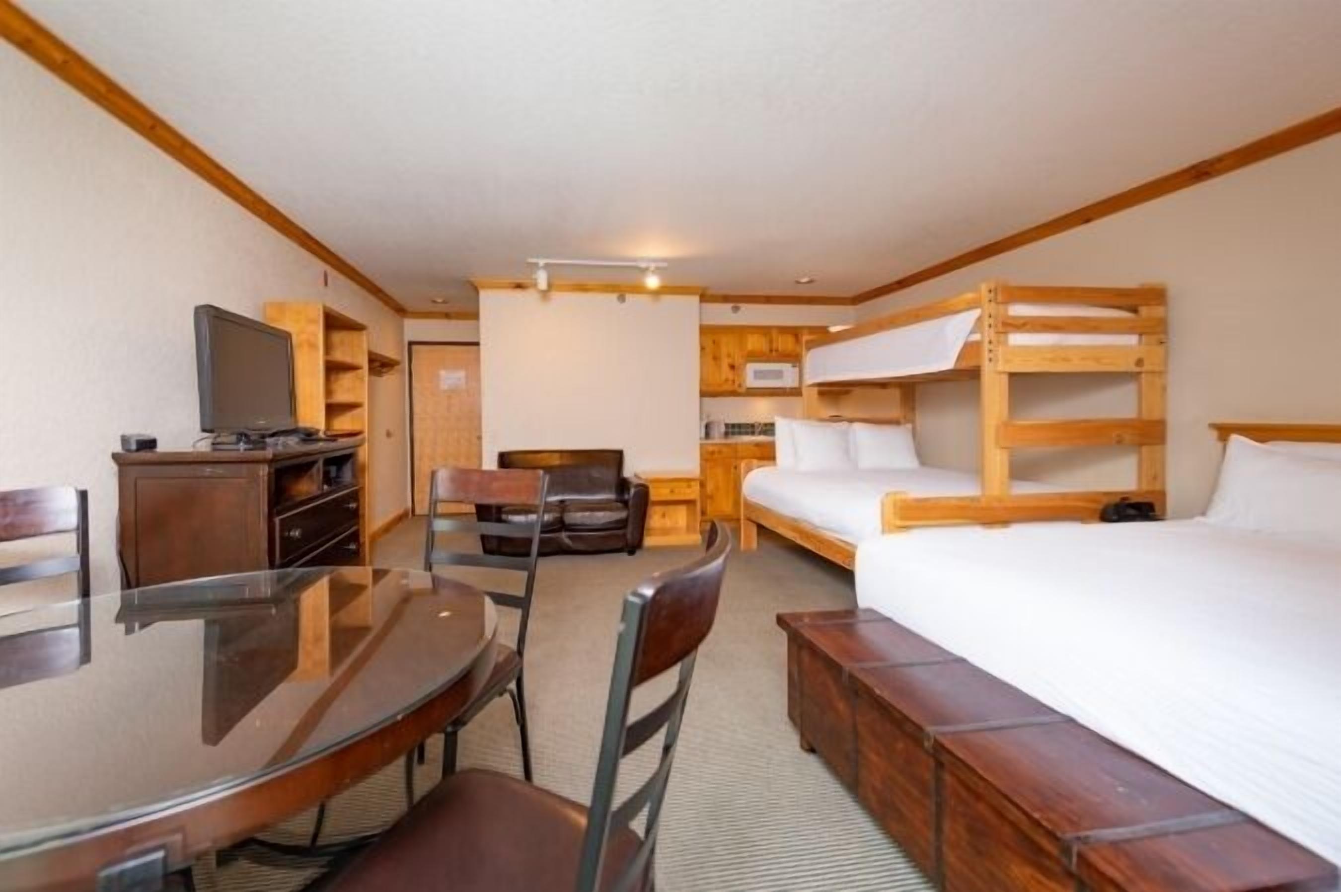 A compact hotel room with a bunk bed, a small dining table with chairs, a television, and a kitchenette.