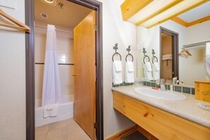 A bathroom with a wooden vanity, a sink, a mirror, and a shower area. - Selkirk Lodge (Sandpoint)