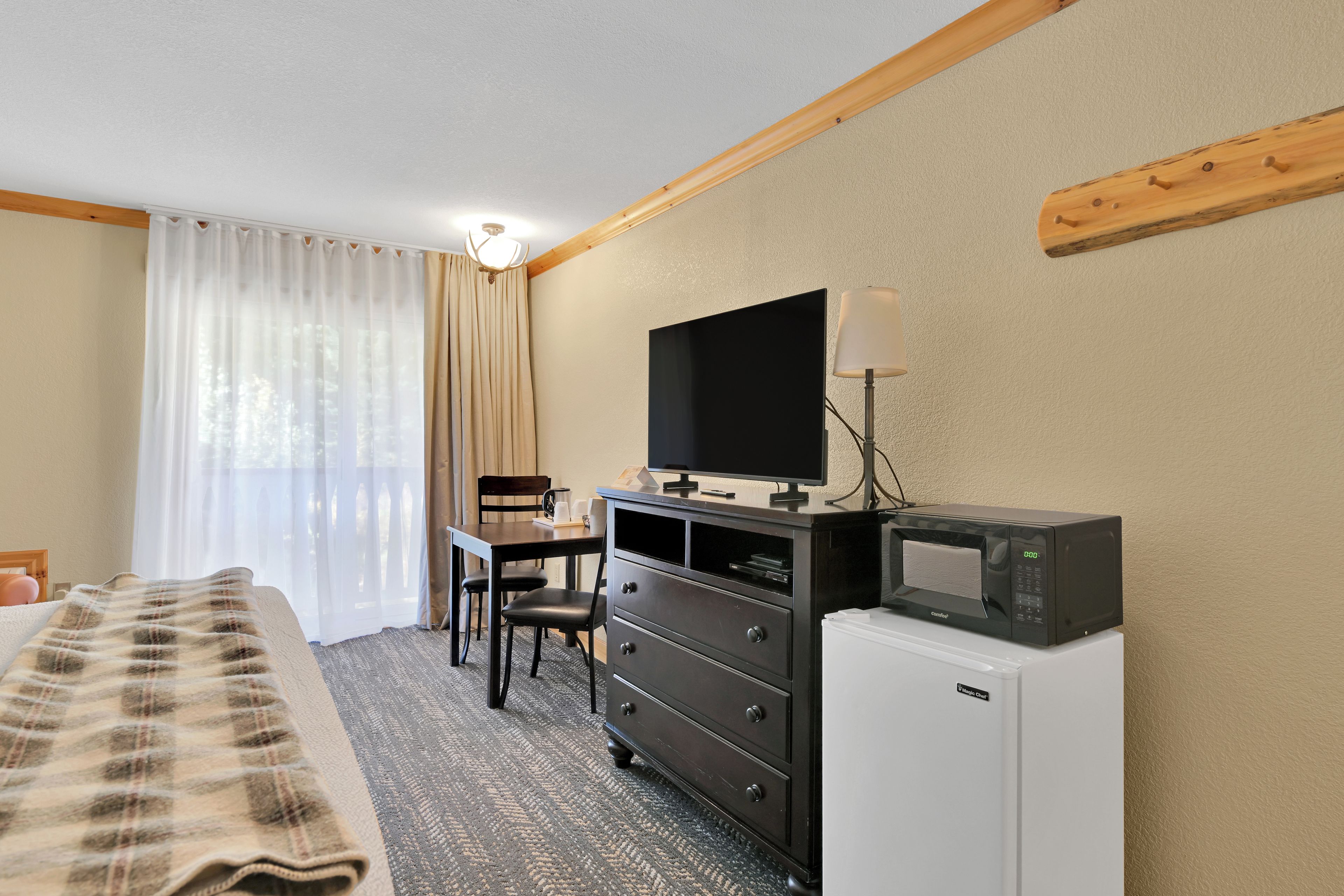 A hotel room with a bed, a desk with a chair, a television, a microwave, and a small refrigerator.
