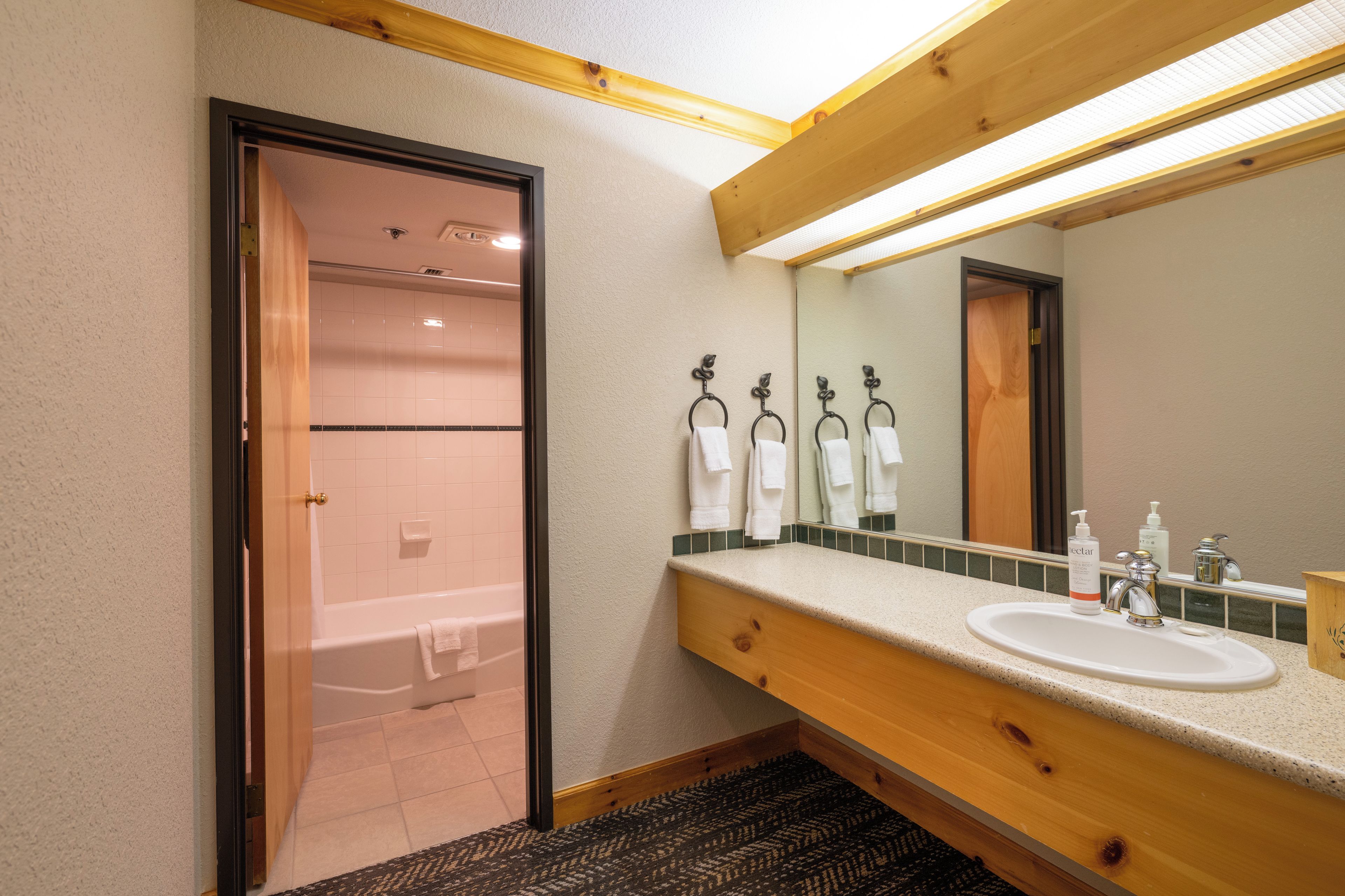 A hotel bathroom with a wooden vanity, a sink, a mirror, and a shower area.