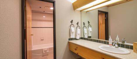 A hotel bathroom with a wooden vanity, a sink, a mirror, and a shower area.