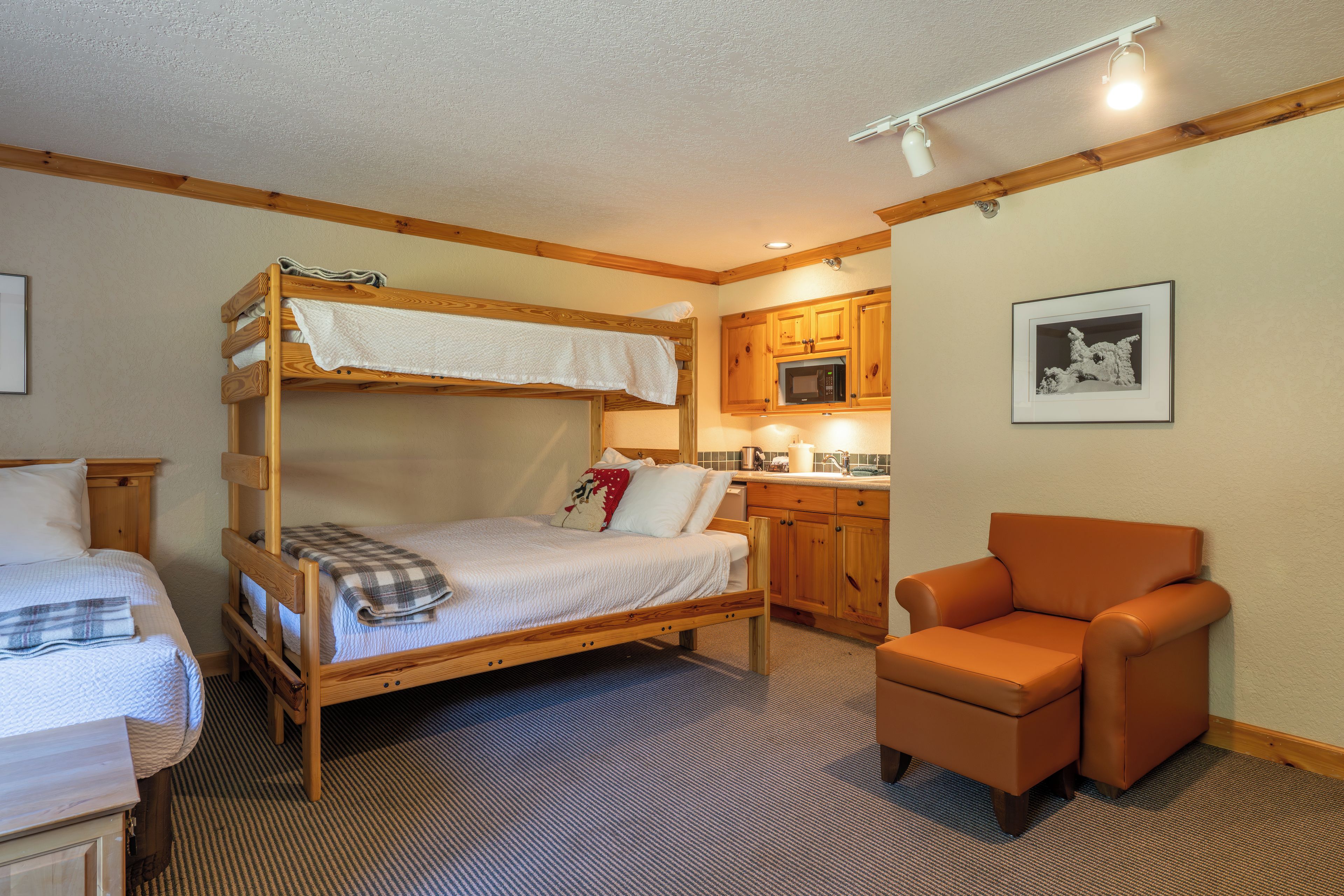 A bunk bed with a kitchen area, a single bed, and a chair.