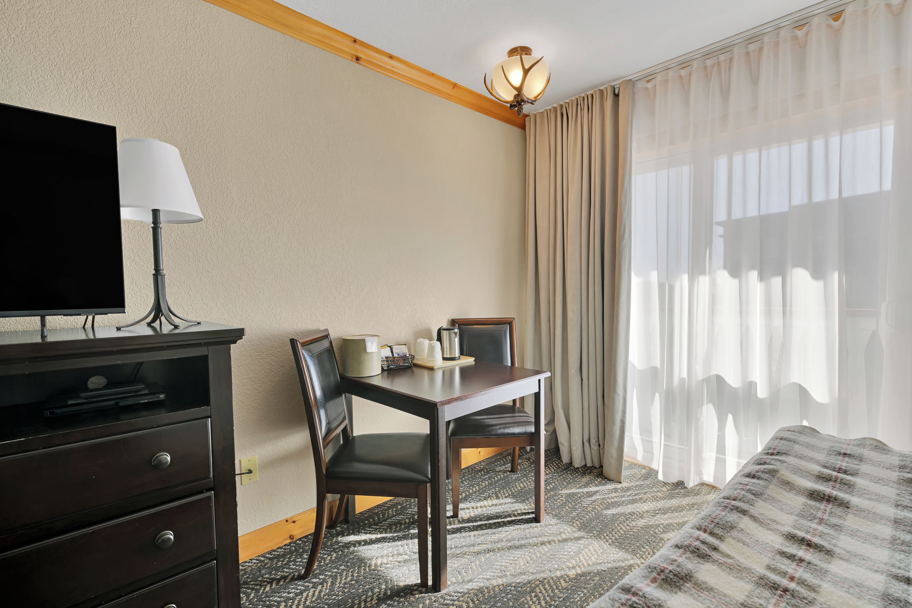 Habitación de hotel con una cama, un escritorio con lámpara, televisión, una silla y una ventana con cortinas.