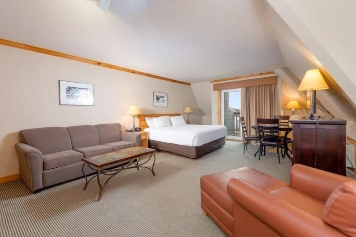 A hotel room with a bed, two sofas, a coffee table, and a desk with lamps.