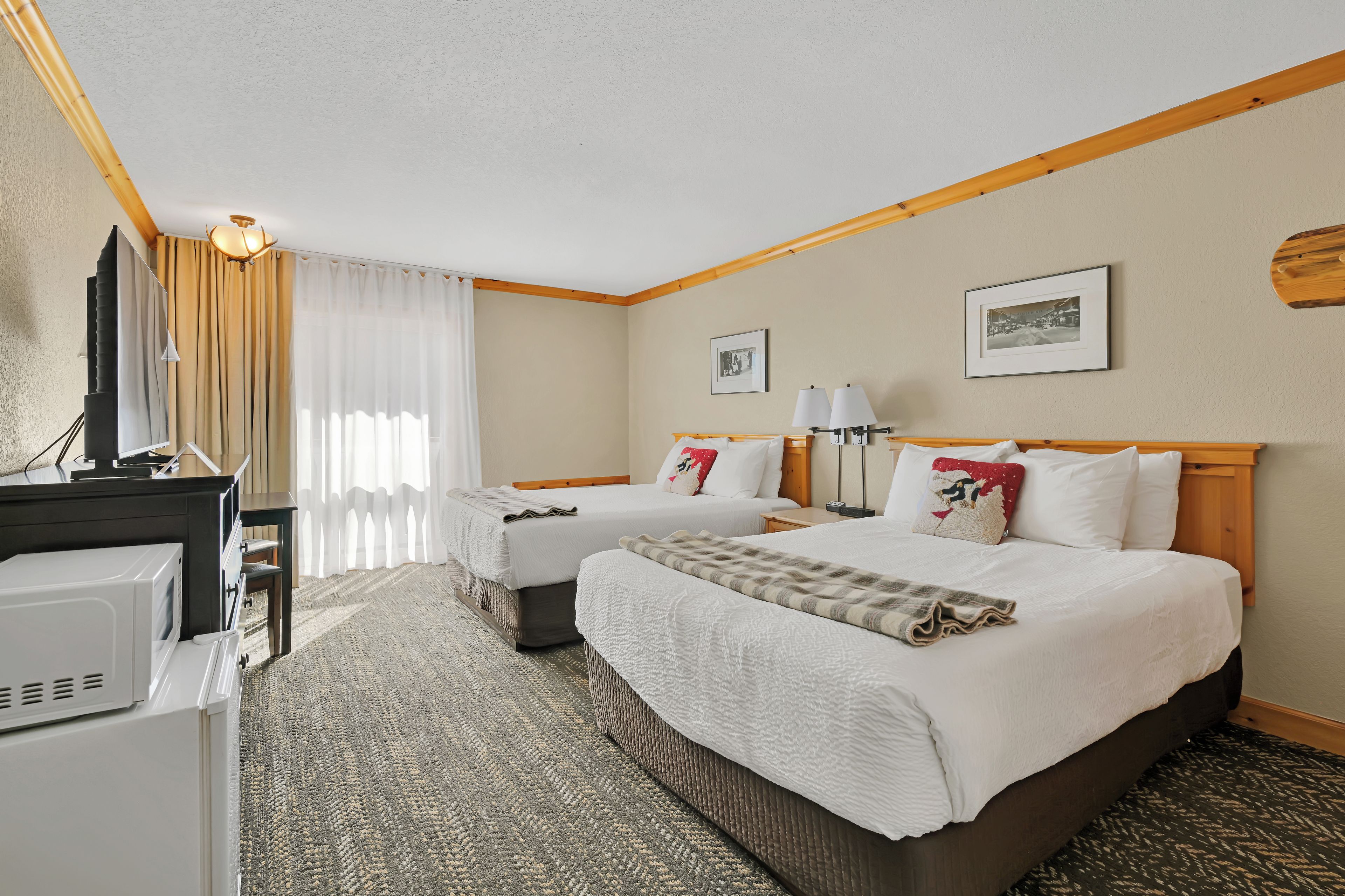 Une chambre d’hôtel avec un grand lit, un lit plus petit, un bureau avec un ordinateur, une télévision et un four à micro-ondes.