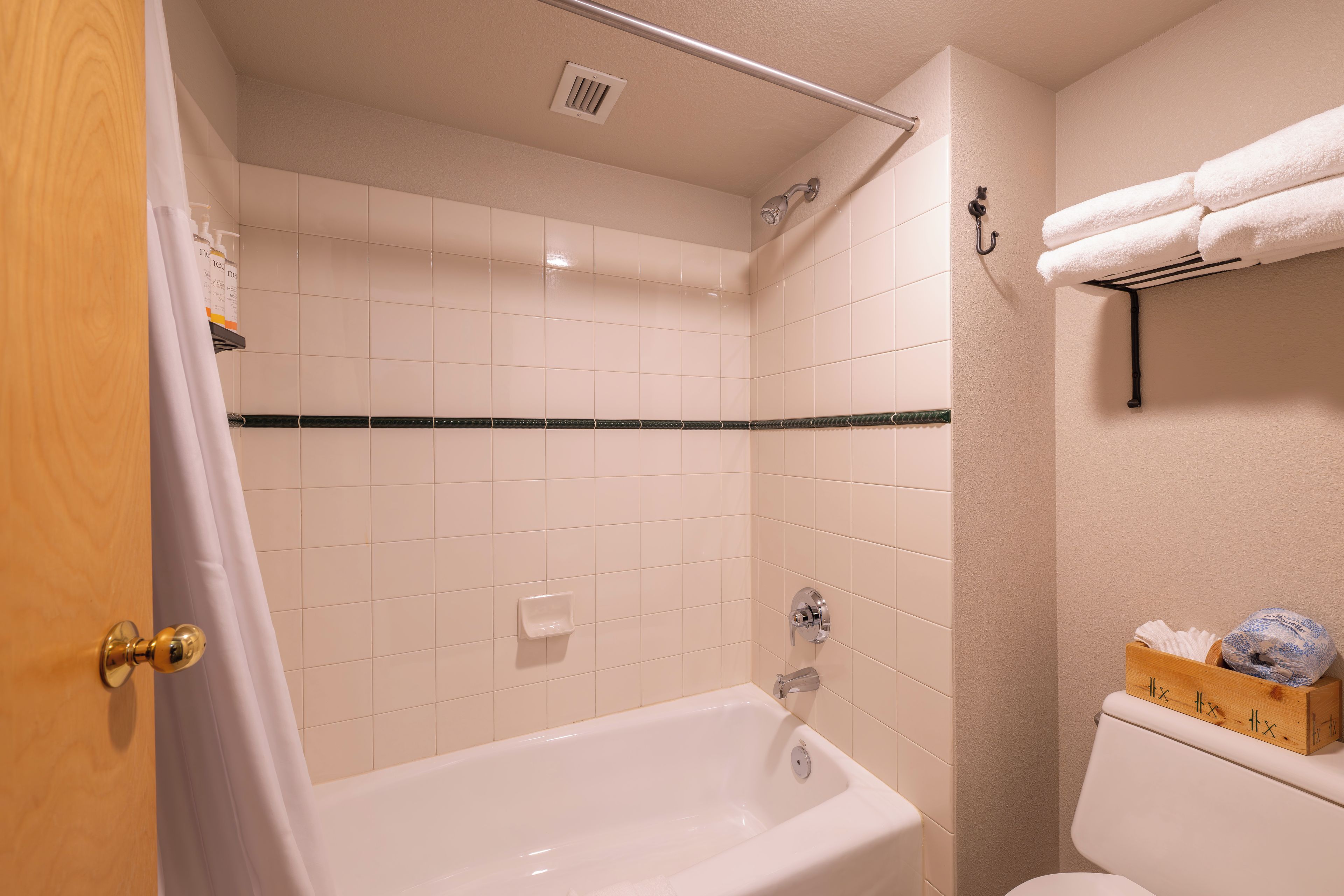 A bathroom with a bathtub, a shower, and a toilet. There is a towel rack with a towel and a box of toiletries.
