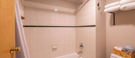 A bathroom with a bathtub, a shower, and a toilet. There is a towel rack with a towel and a box of toiletries.