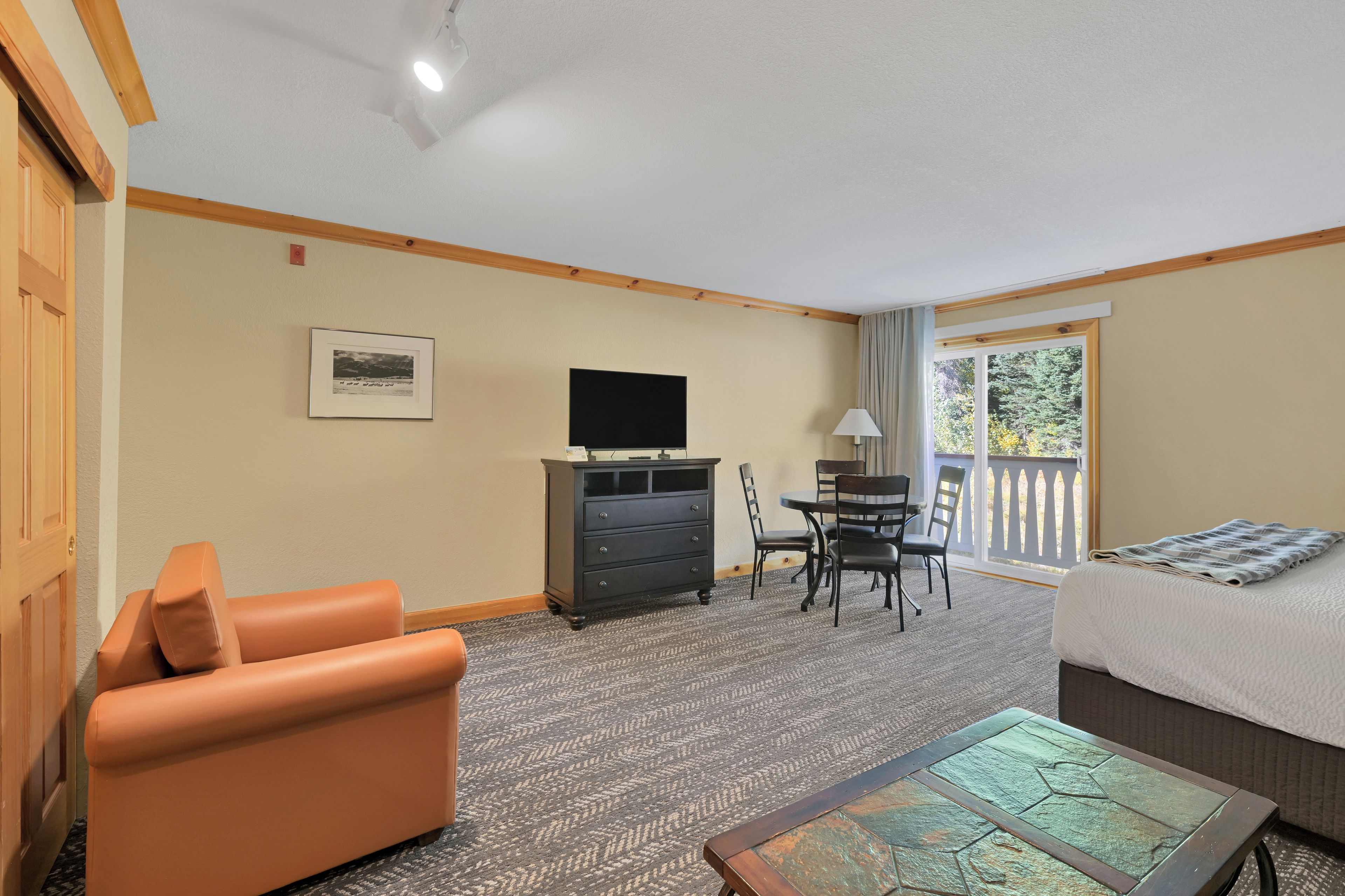 A hotel room with a sofa, a television, a desk with chairs, and a bed.