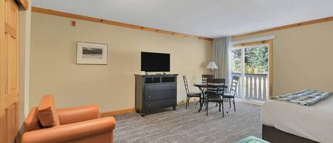 A hotel room with a sofa, a television, a desk with chairs, and a bed.