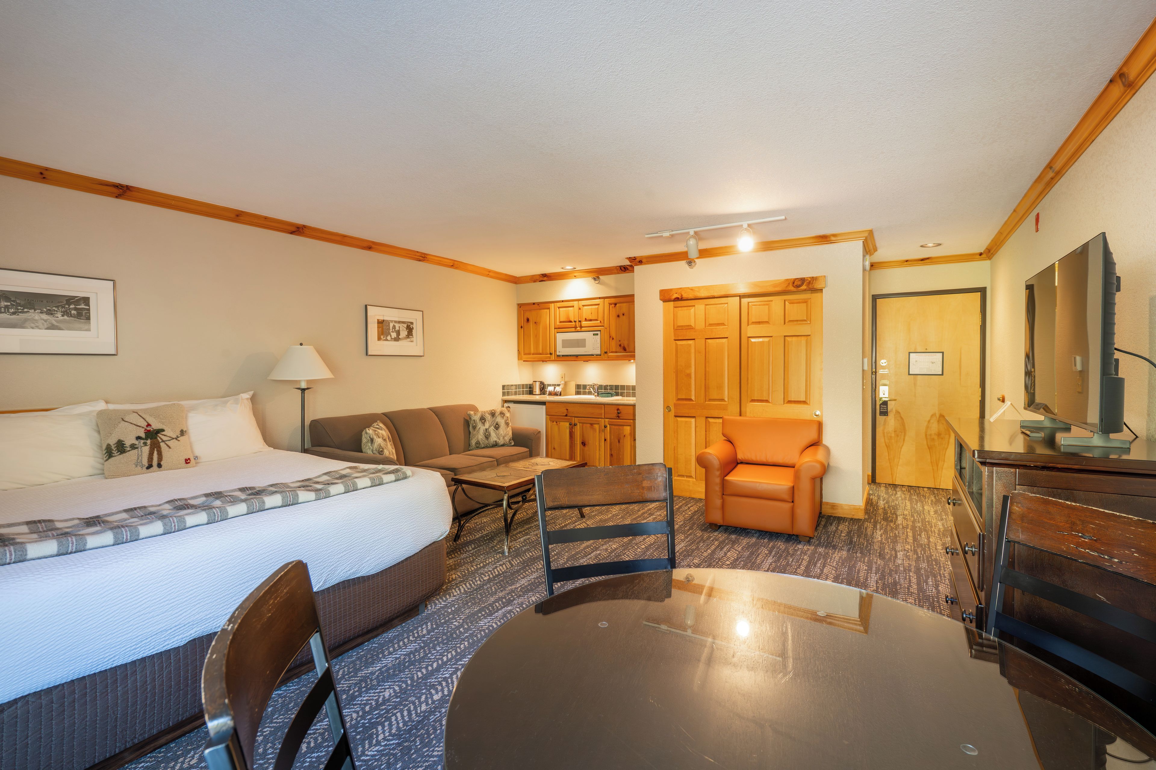 A hotel room with a bed, a sofa, a dining table, a chair, a kitchen area, and a bathroom.