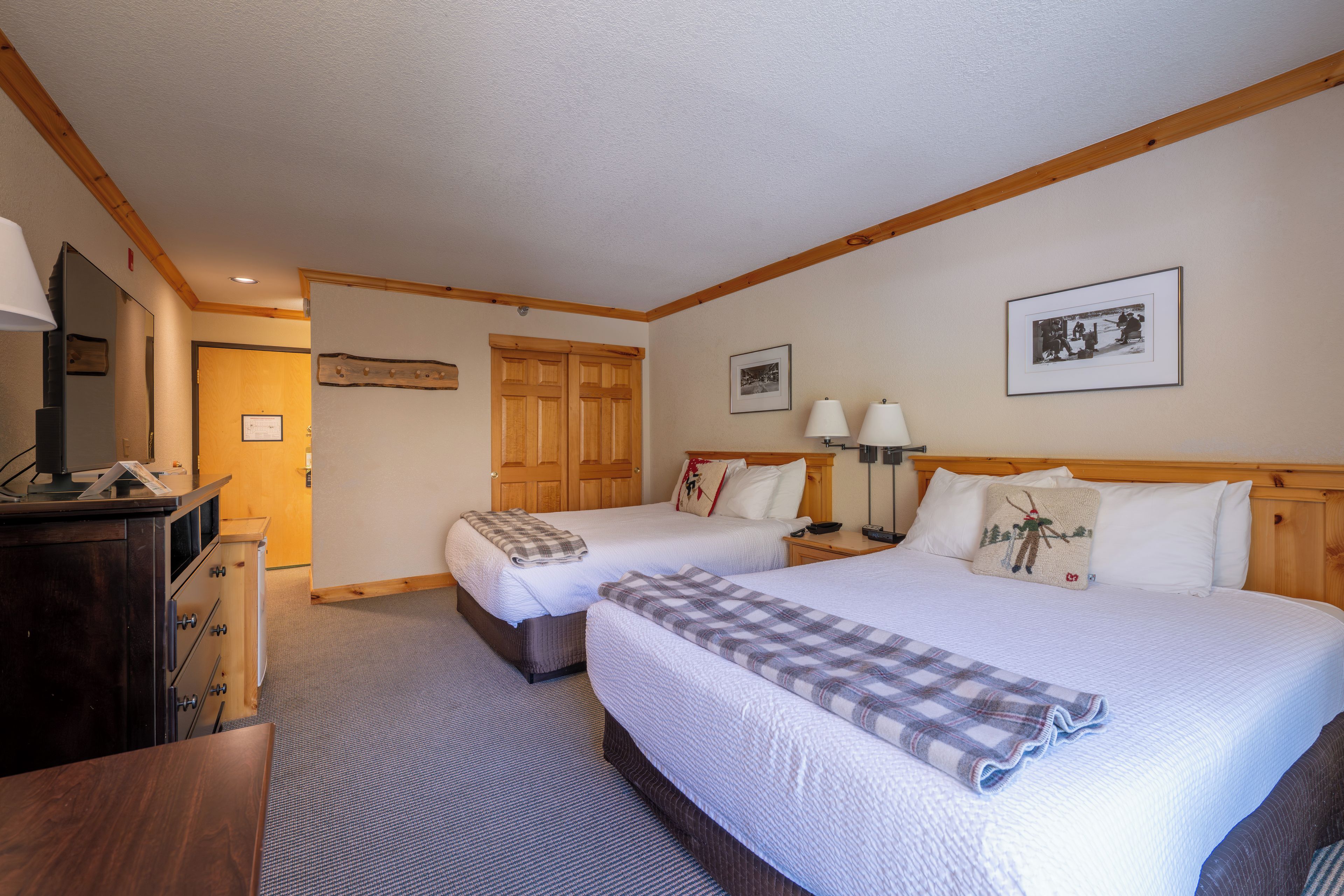 A hotel room with two beds, a wooden headboard, a desk with a lamp, and a television.