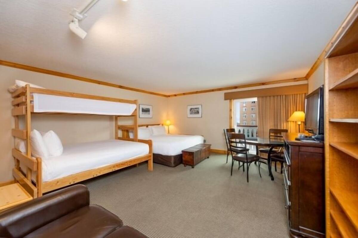 A hotel room with two bunk beds, a desk, a chair, and a television.