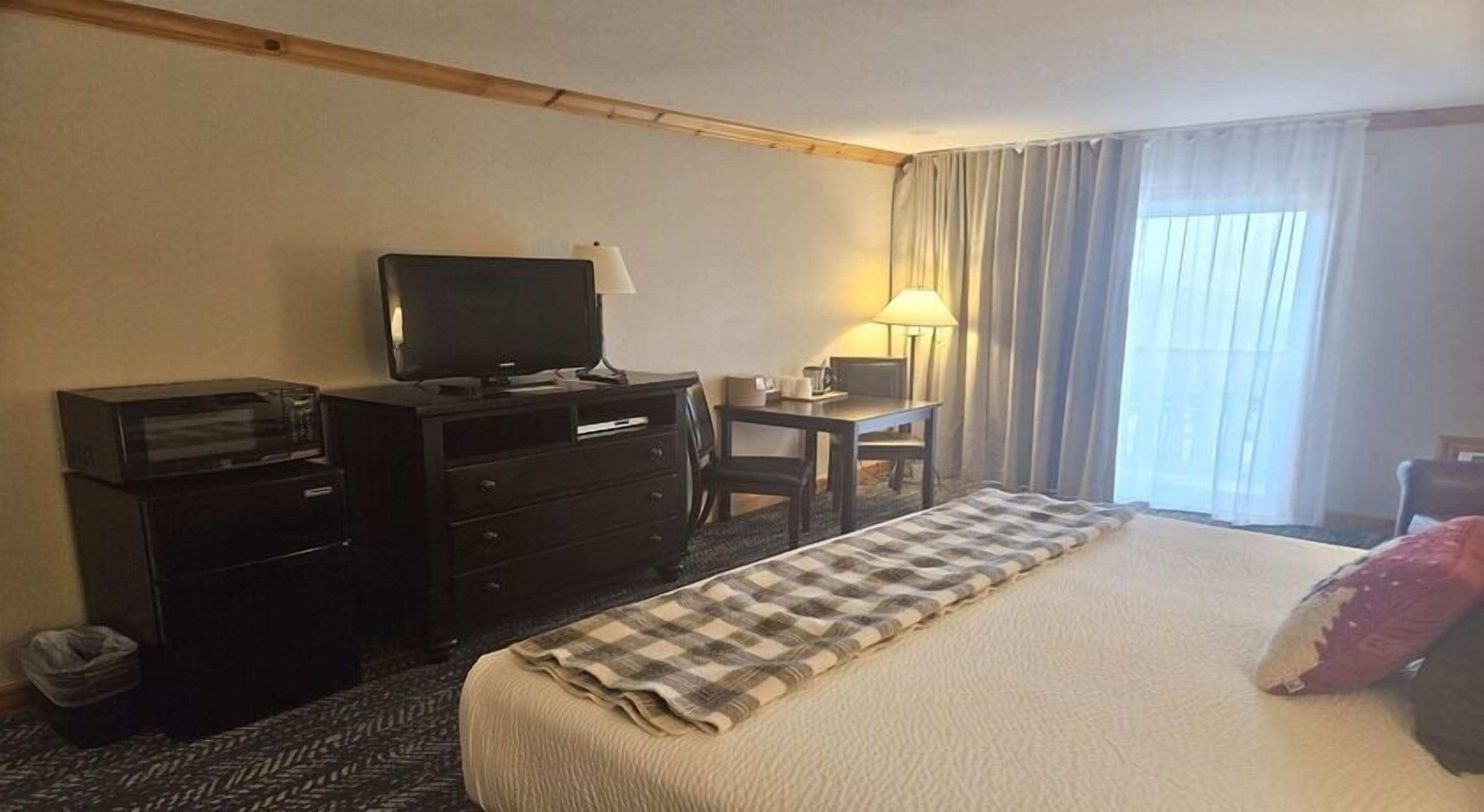 A hotel room with a bed, a desk with a lamp, a television, and a trash bin.