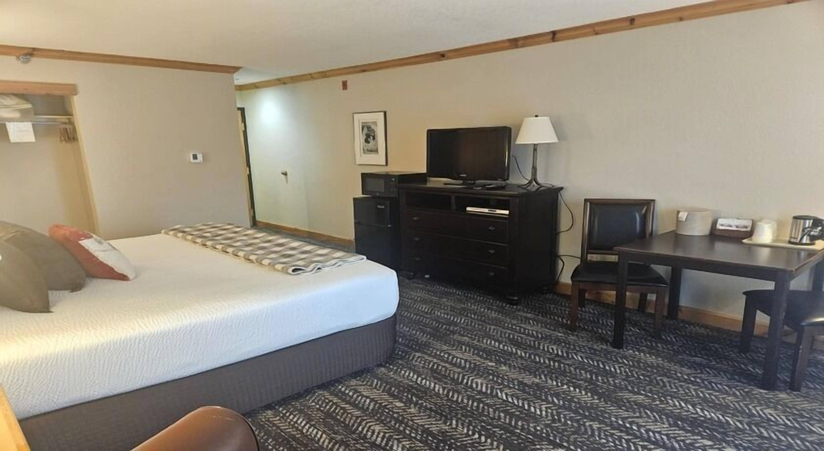 A hotel room with a bed, a desk, a chair, a television, and a dresser.