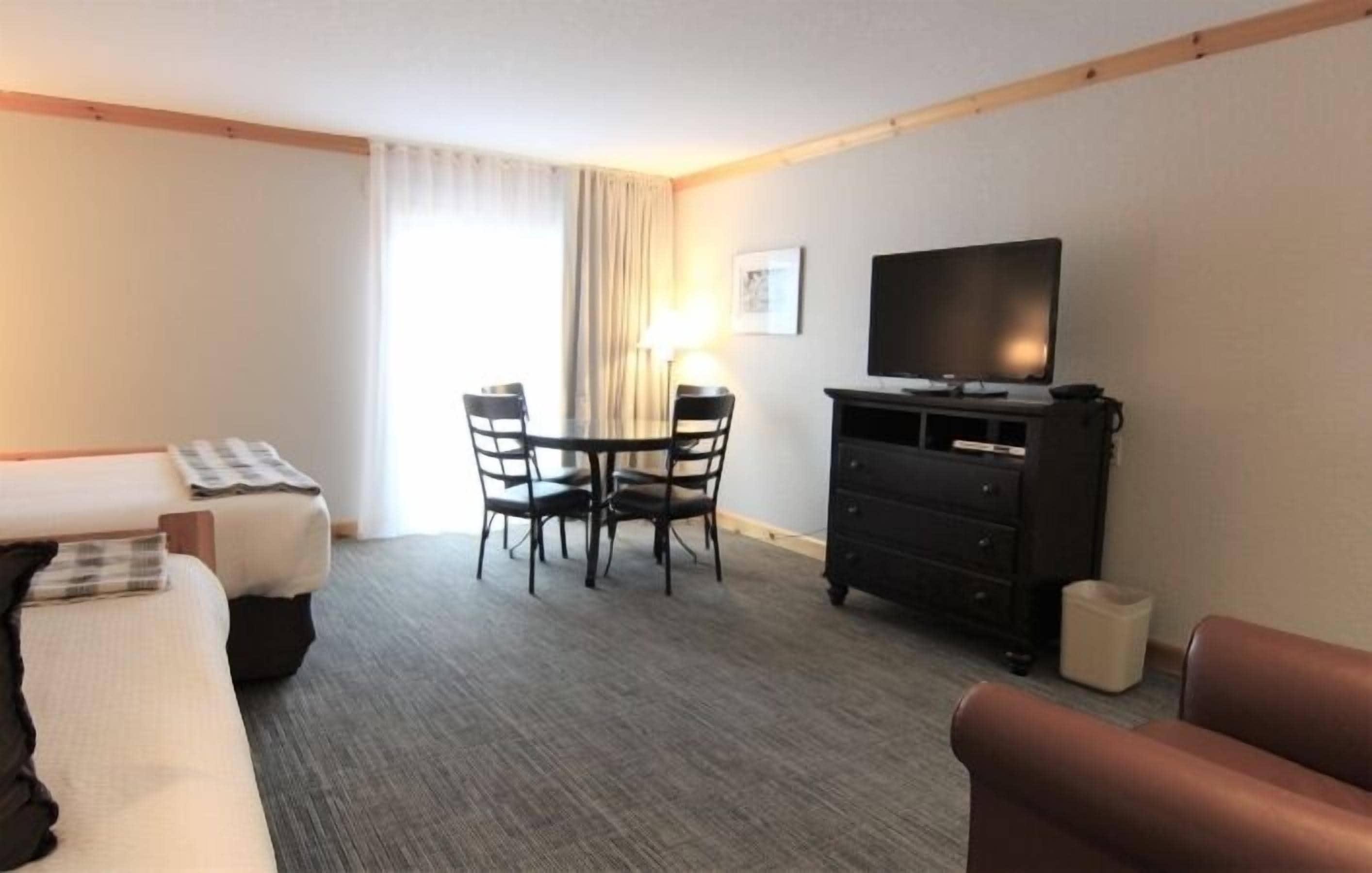 A hotel room with a bed, a desk with a chair, a television, and a small table with chairs.