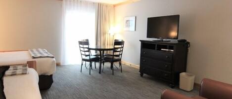A hotel room with a bed, a desk with a chair, a television, and a small table with chairs.