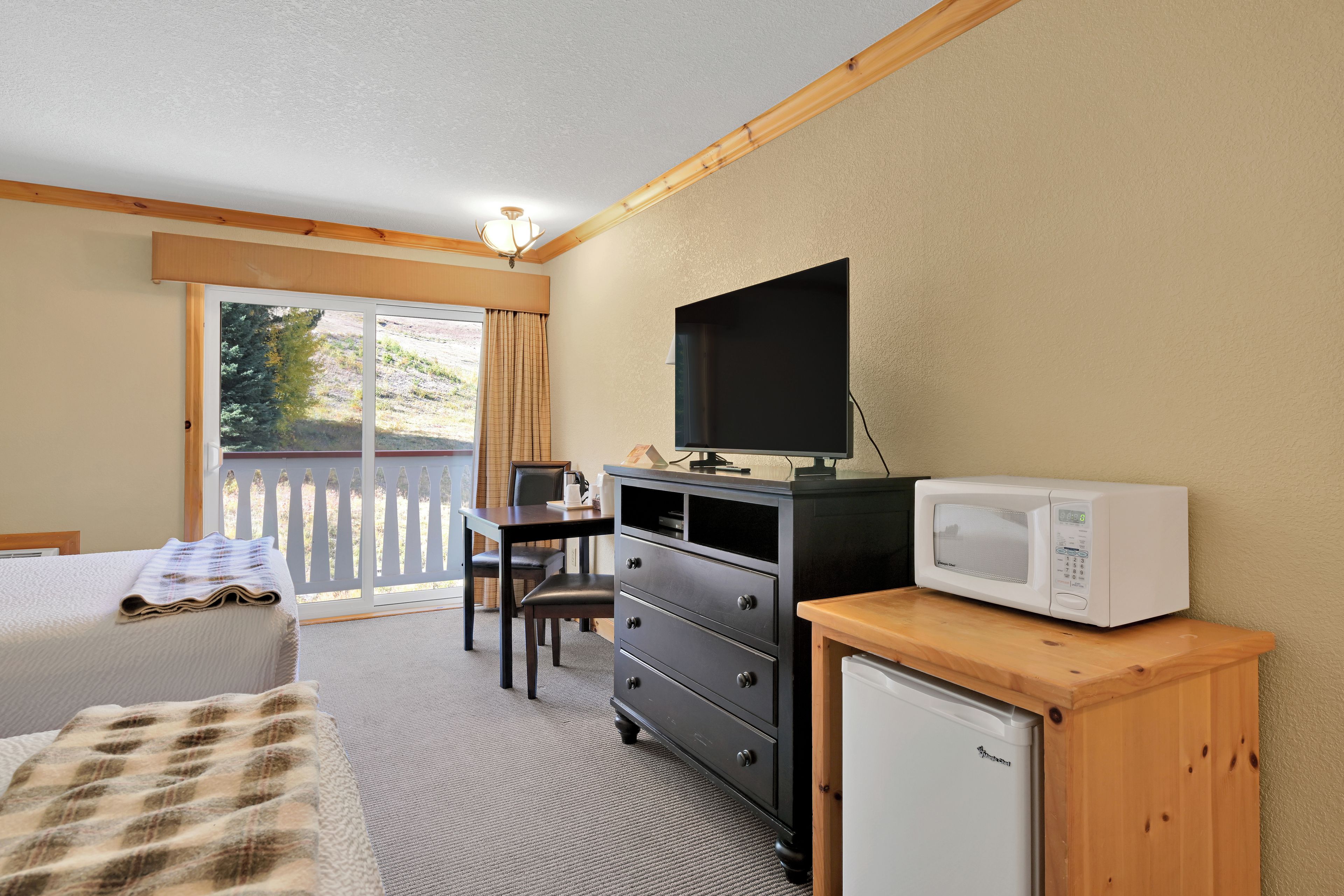 Quarto de hotel com cama, escrivaninha, televisão, micro-ondas e pequeno frigorífico.