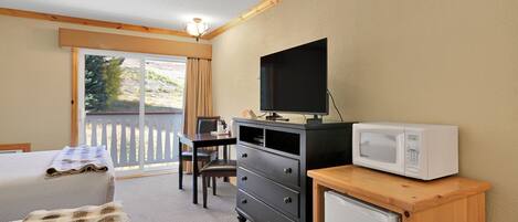 Quarto de hotel com cama, escrivaninha, televisão, micro-ondas e pequeno frigorífico.