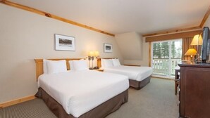 Une chambre d’hôtel avec deux lits, une tête de lit en bois, un bureau avec une lampe et une fenêtre donnant sur des arbres.
